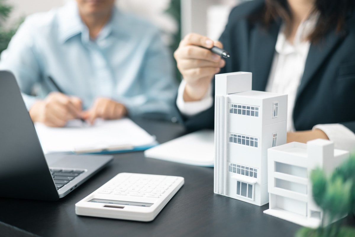 Dois profissionais analisando documentos com maquete de prédio sobre a mesa, indicando negociação de imóveis.