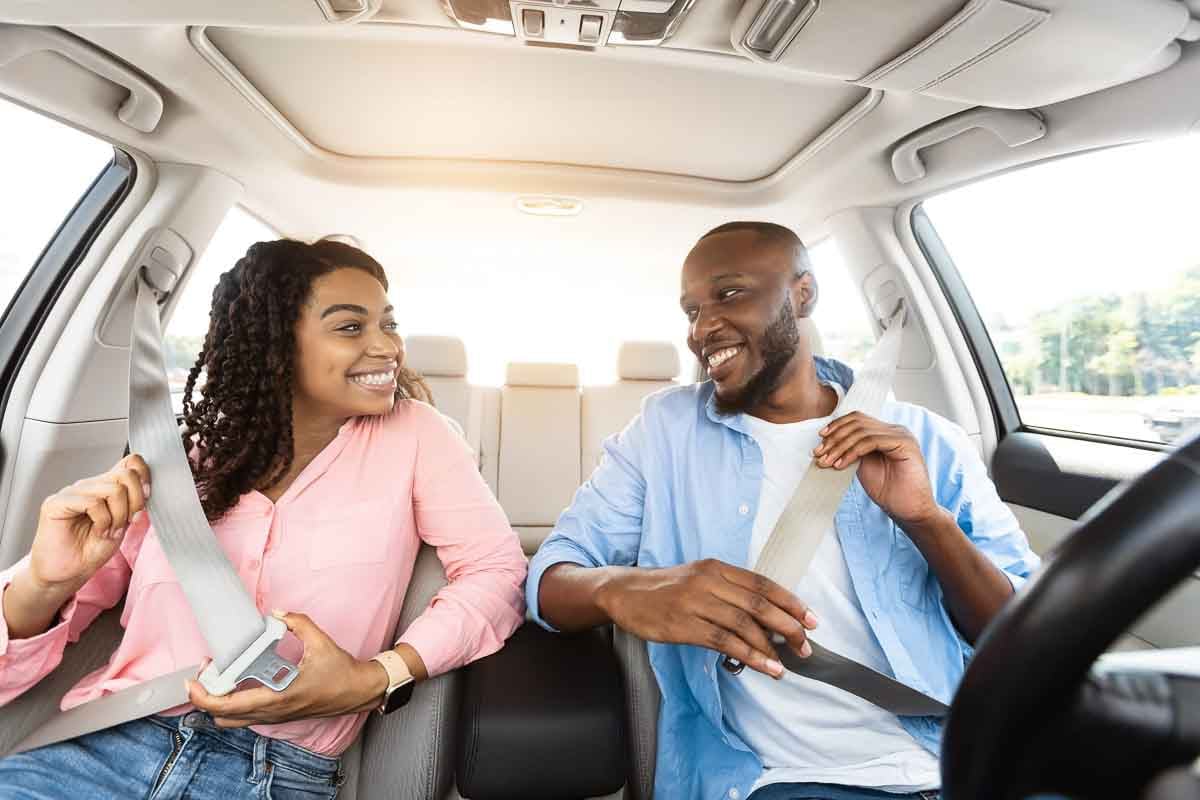 Casal contente afivelando o cinto de segurança em um carro.