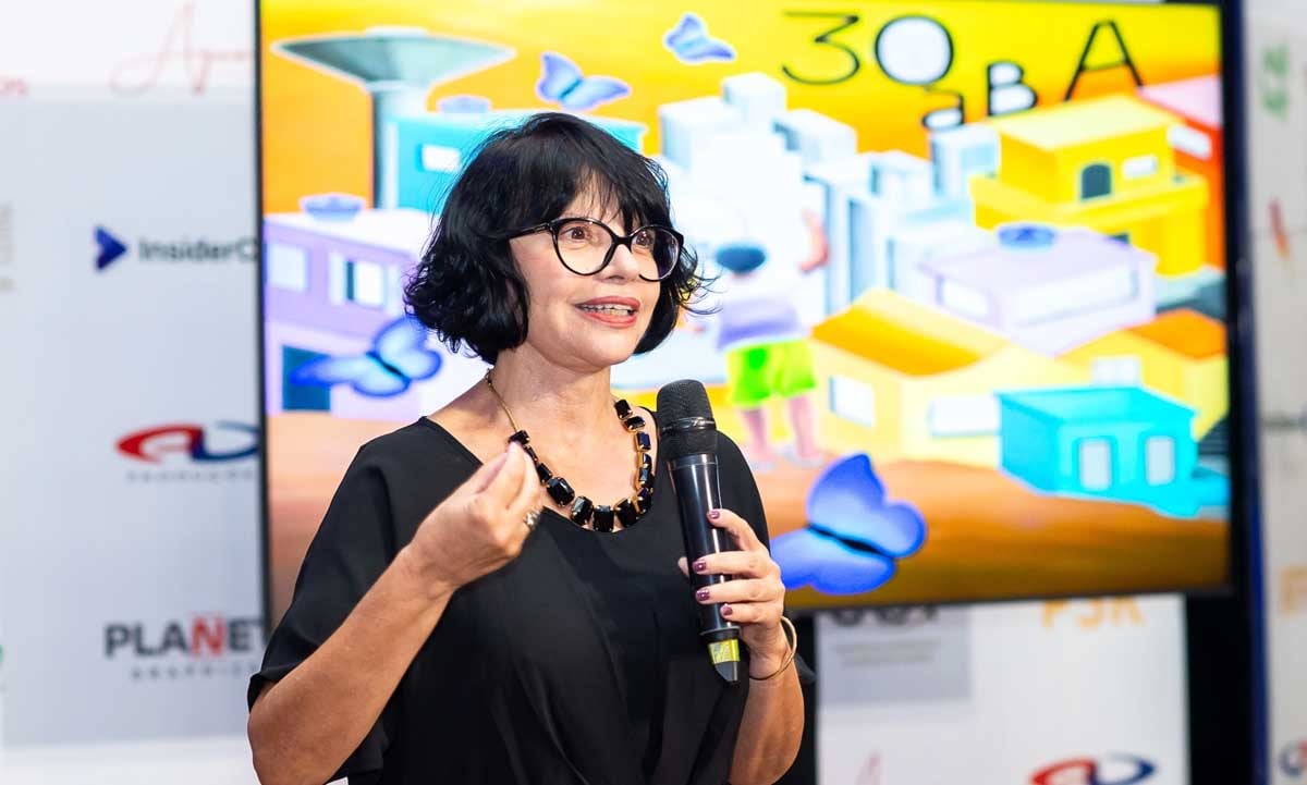 Mulher apresentando uma palestra com uma tela colorida com ilustrações ao lado.