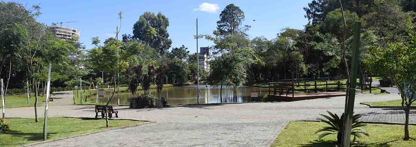 Parque arborizado com lago e caminhos de pedra.