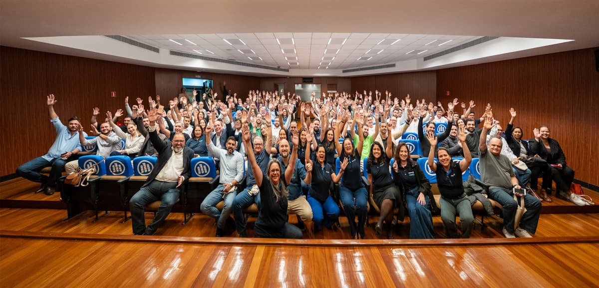 Grupo de corretores reunidos em auditório, sorrindo e com braços erguidos em gesto de celebração.