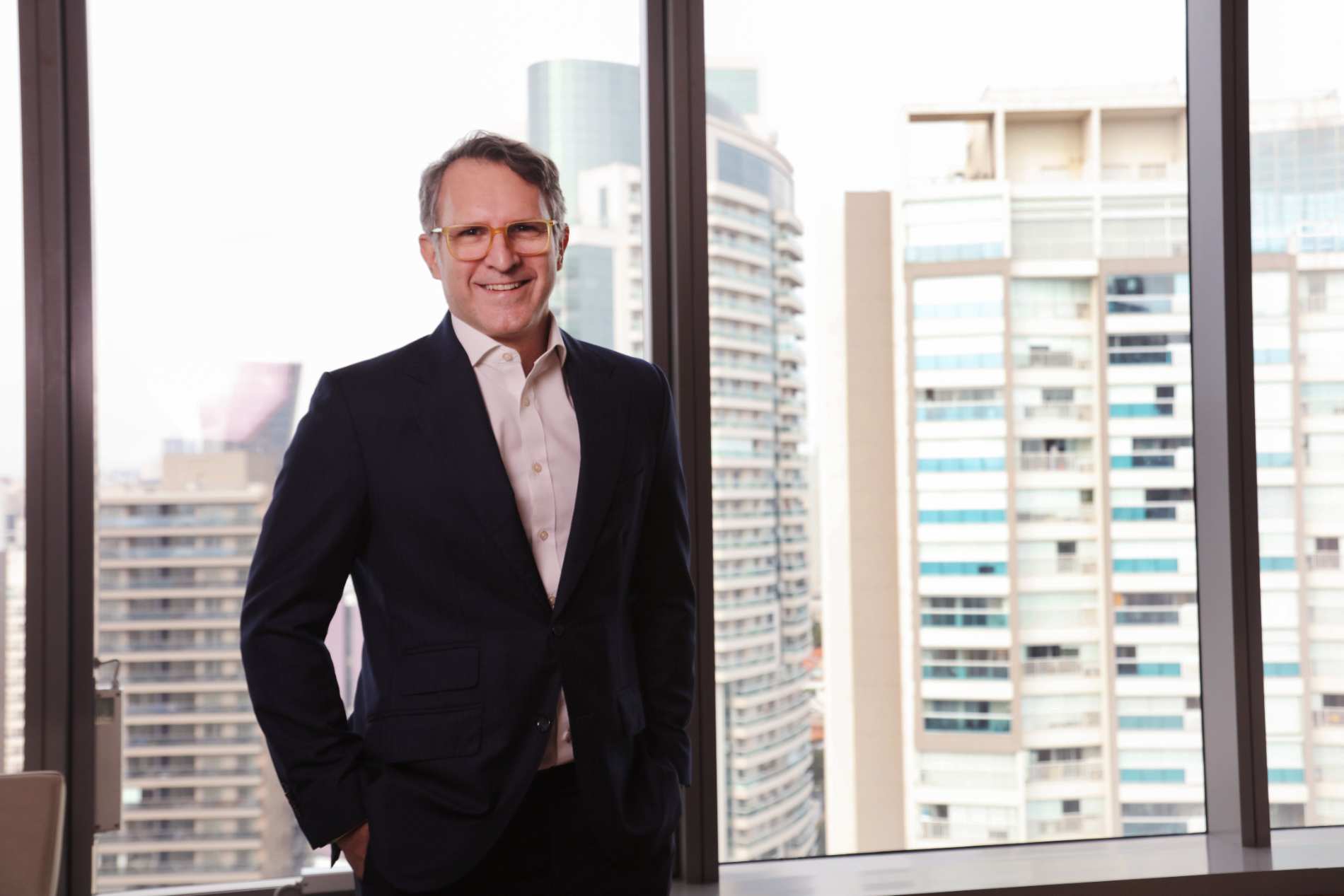 Pessoa em ambiente corporativo, em frente a janelas com vista para prédios comerciais, representando análise e gestão de riscos empresariais.