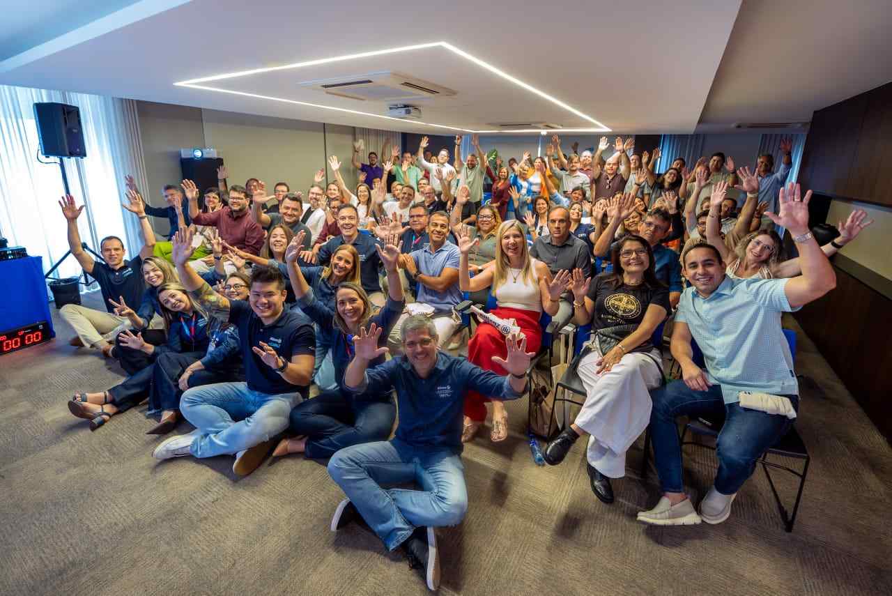 Grupo de profissionais reunidos em auditório durante treinamento da Allianz, com participantes em pé e braços erguidos ao final do evento.