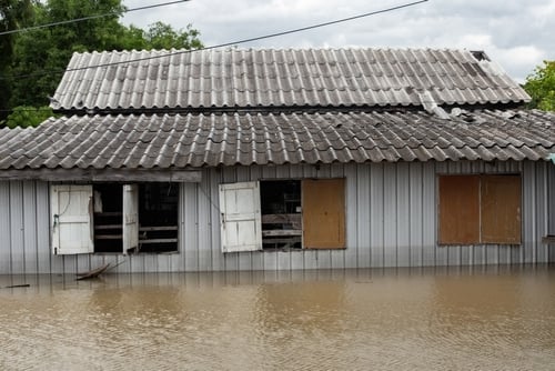 Casa danificada com janelas abertas parcialmente submersa em água de enchente.