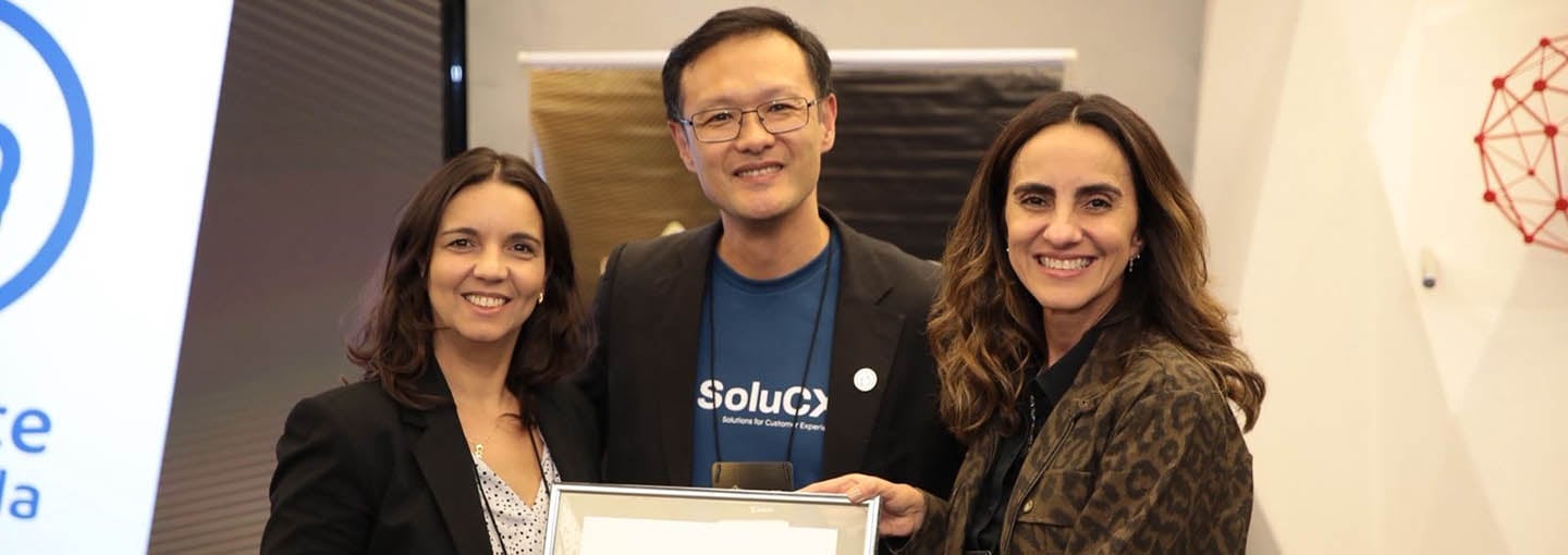 Superintendente e Diretora Executiva de Marketing segurando placa do selo “O Cliente Recomenda” ao lado de representante da SoluCX.