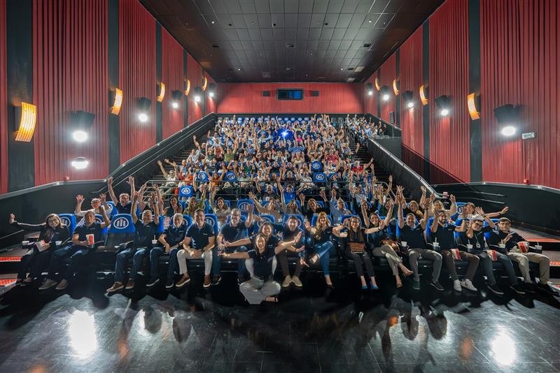 Grupo de profissionais reunidos em sala de treinamento, com participantes sentados e braços levantados durante capacitação promovida pela Allianz.