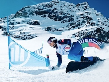 Atleta olímpico de snowboard esquiando em uma montanha de neve    próximo a bandeiras com patrocínio da marca Allianz. 